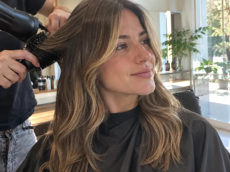 Una clienta sonriendo mientras le secan el pelo en una peluquería.